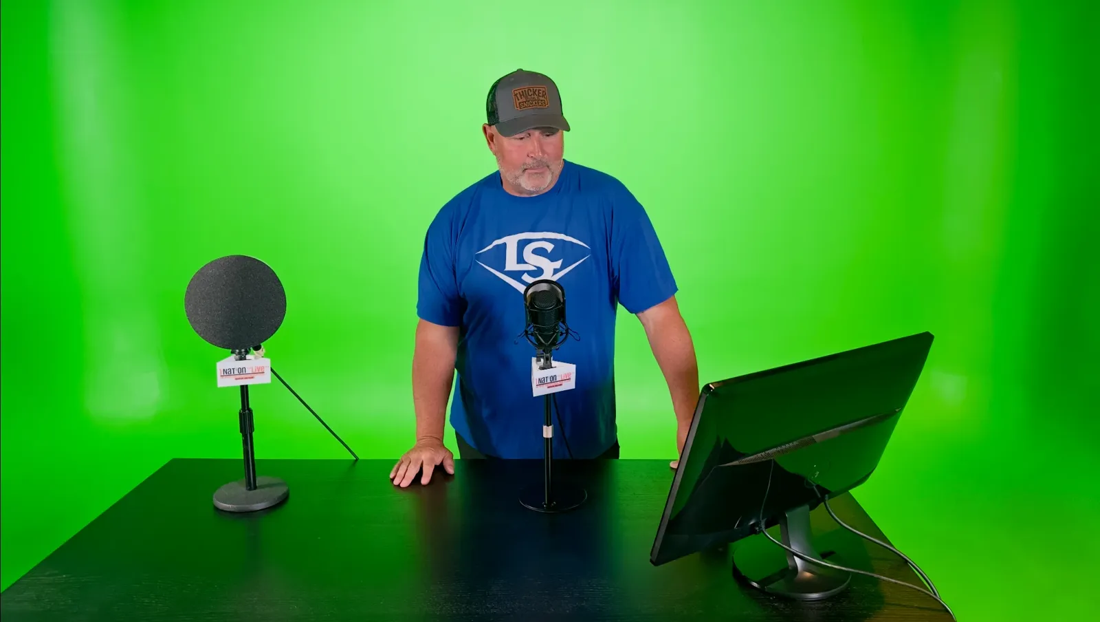 Talent recording at a desk with broadcast microphones and a monitor on the Killerspots green screen set